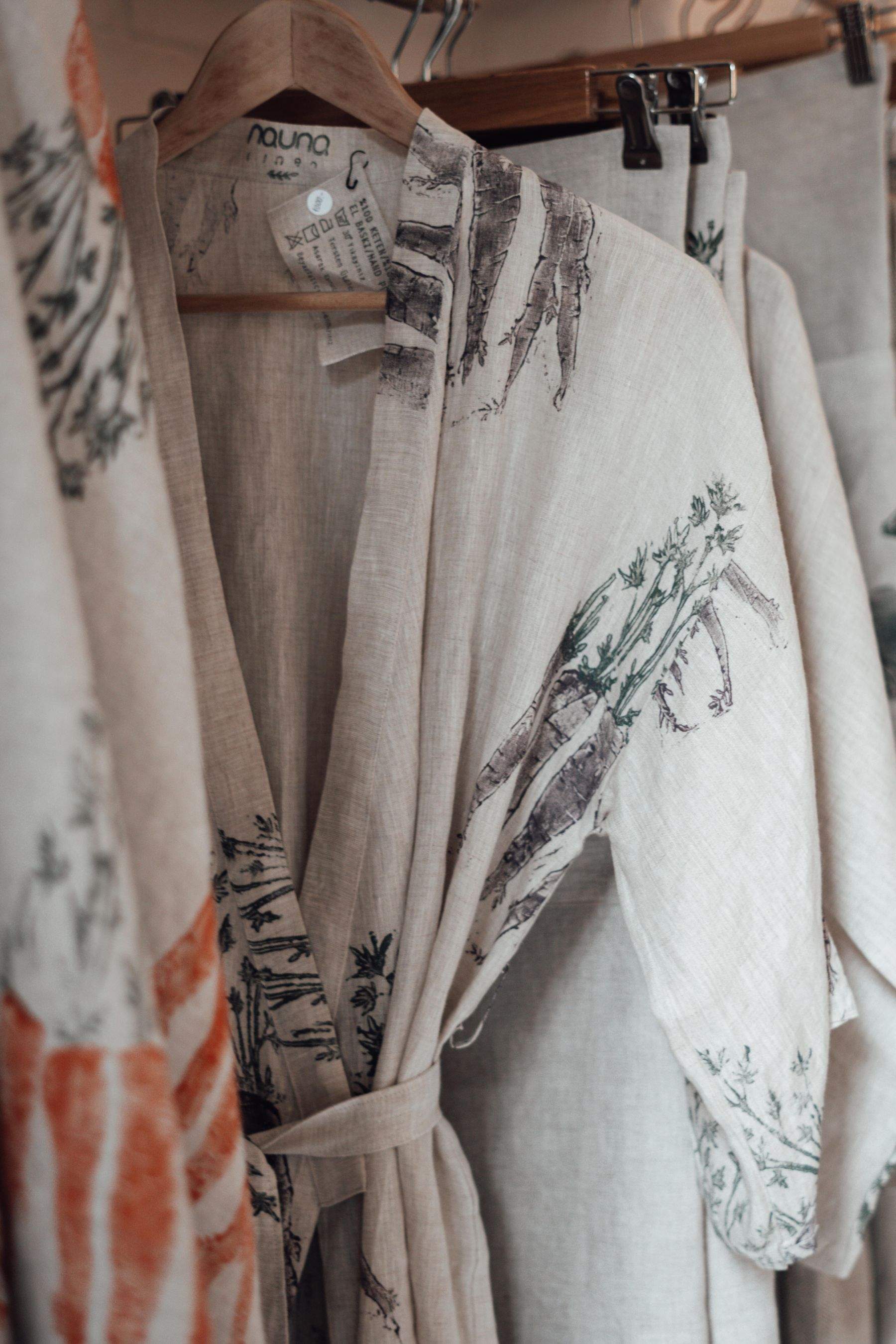 A cream linen robe printed with terracotta and sage botanical sketches, hanging on a rail