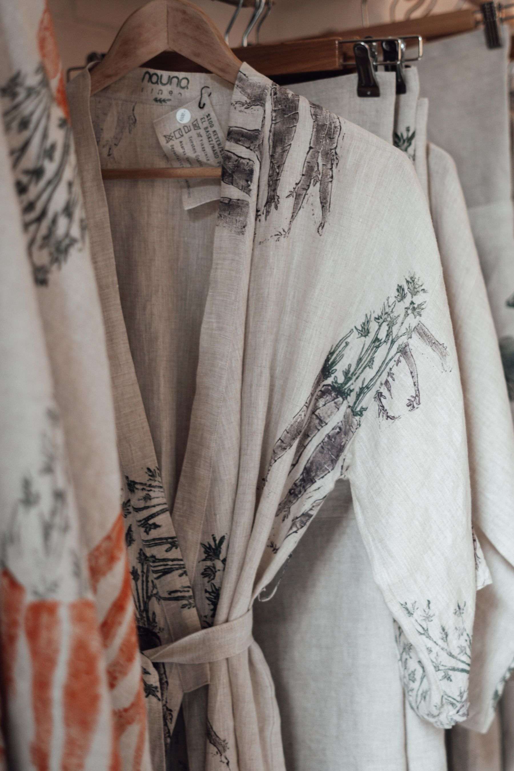 A cream linen robe printed with terracotta and sage botanical sketches, hanging on a rail