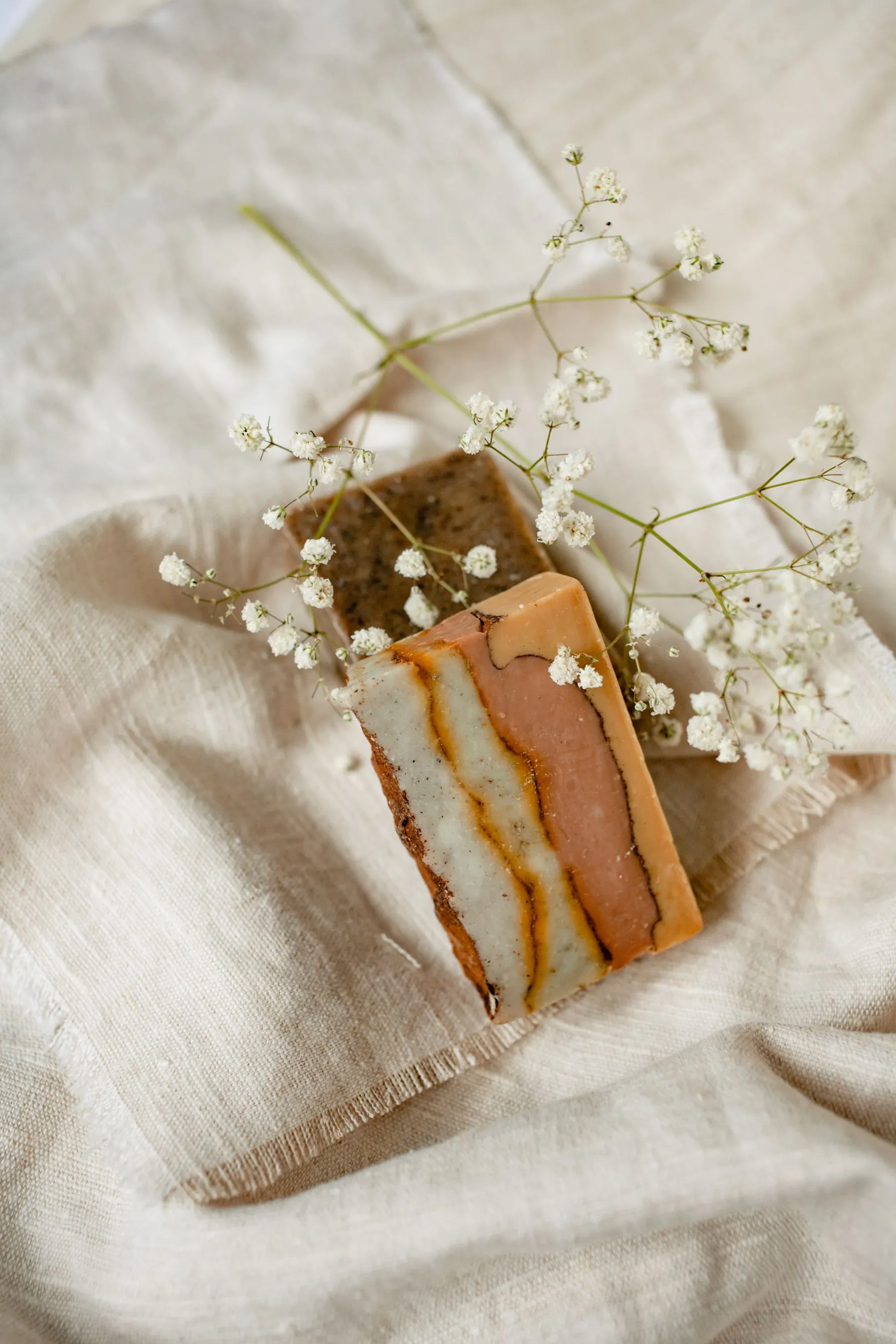 Two bars of handmade soap on linen, scattered with baby’s breath
