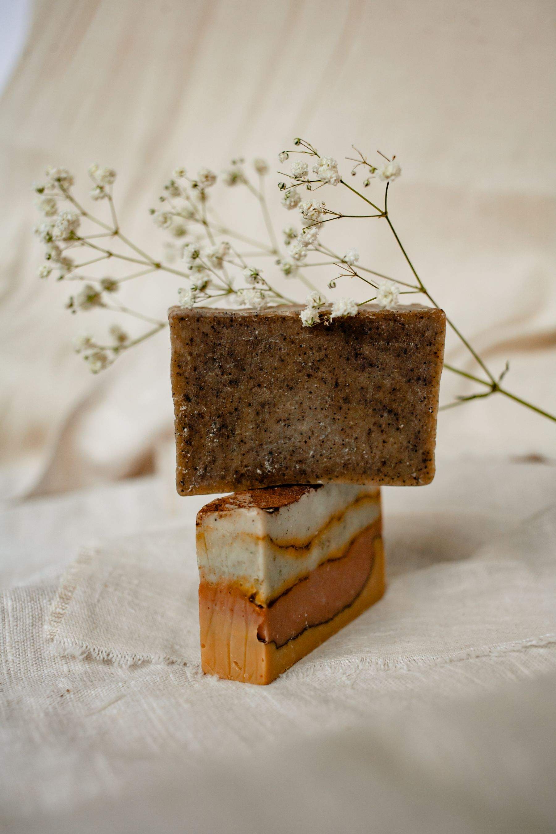 Two stacked bars of handmade soap, one dark and one swirled with terracotta, with sprigs of baby’s breath