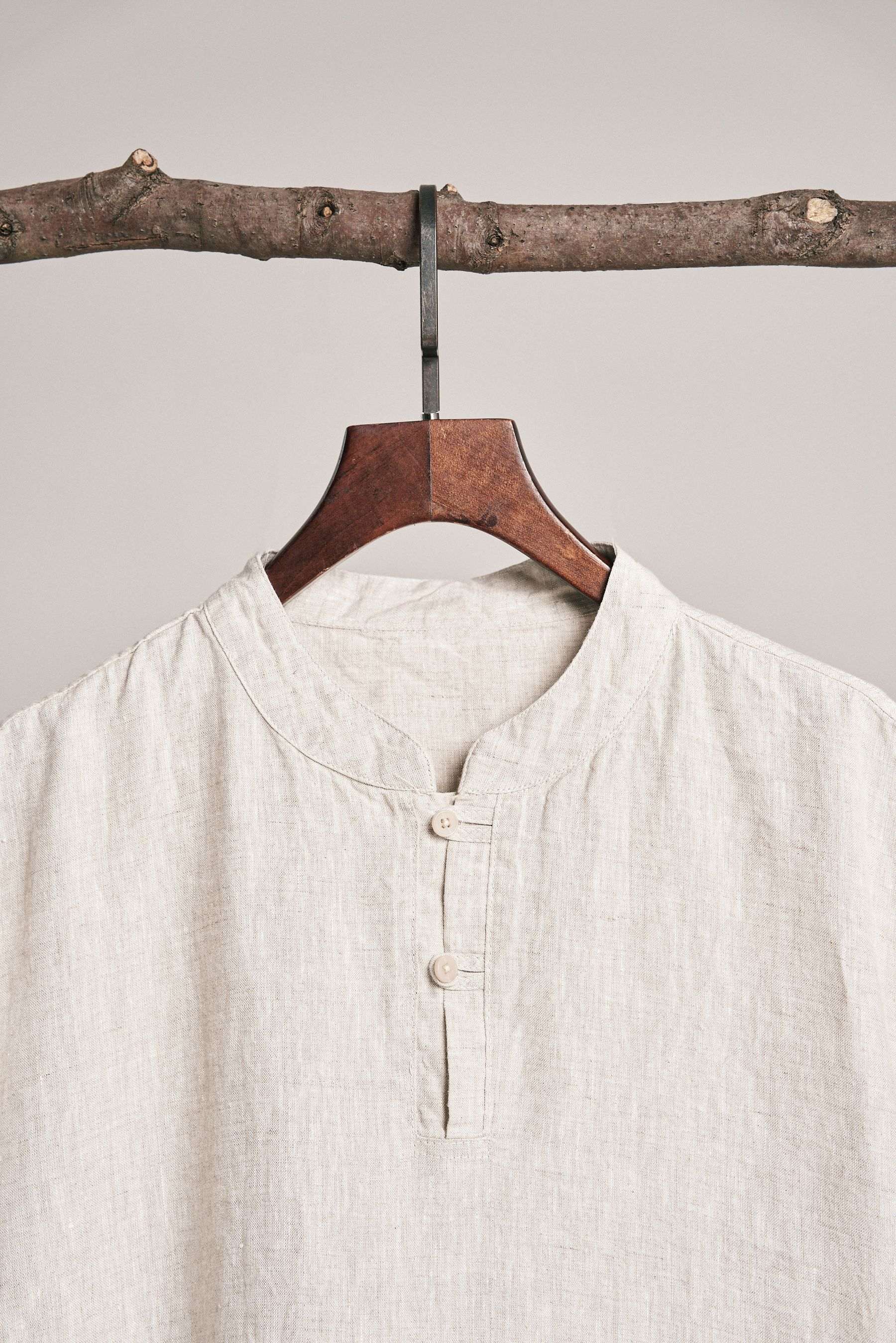 Close view of a cream linen band-collar shirt with three buttons, on a wooden hanger