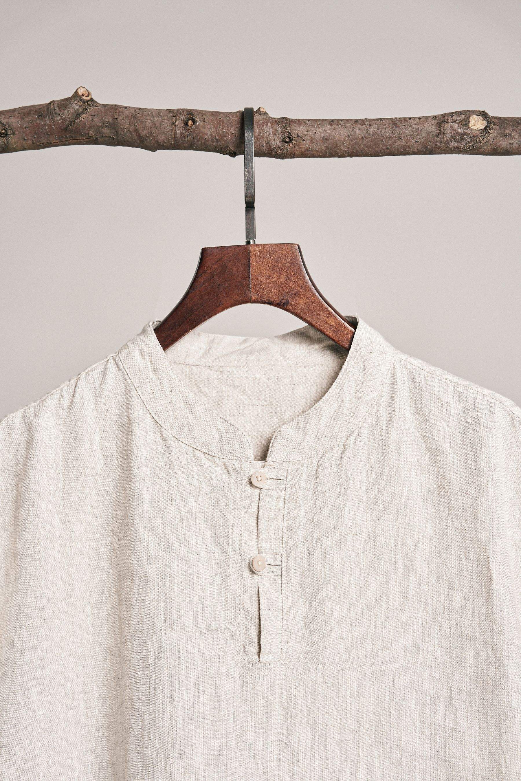 Close view of a cream linen band-collar shirt with three buttons, on a wooden hanger