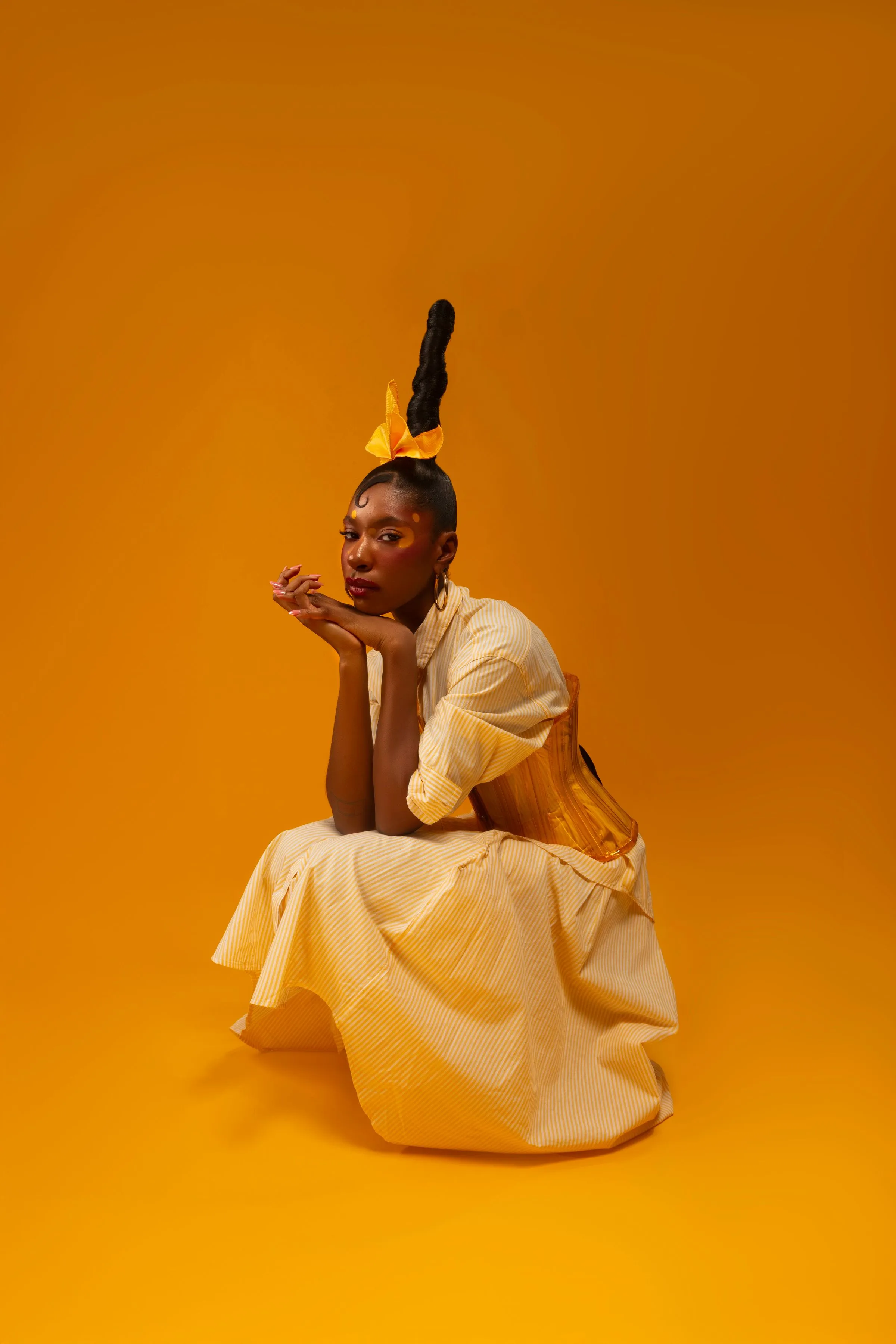 A woman in a cream dress sitting against a bright marigold backdrop