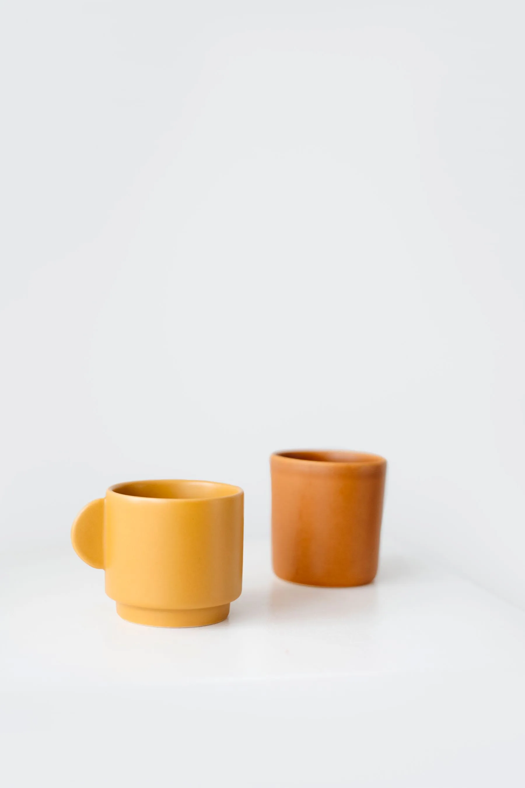 Two small ceramic cups in marigold and burnt orange glazes