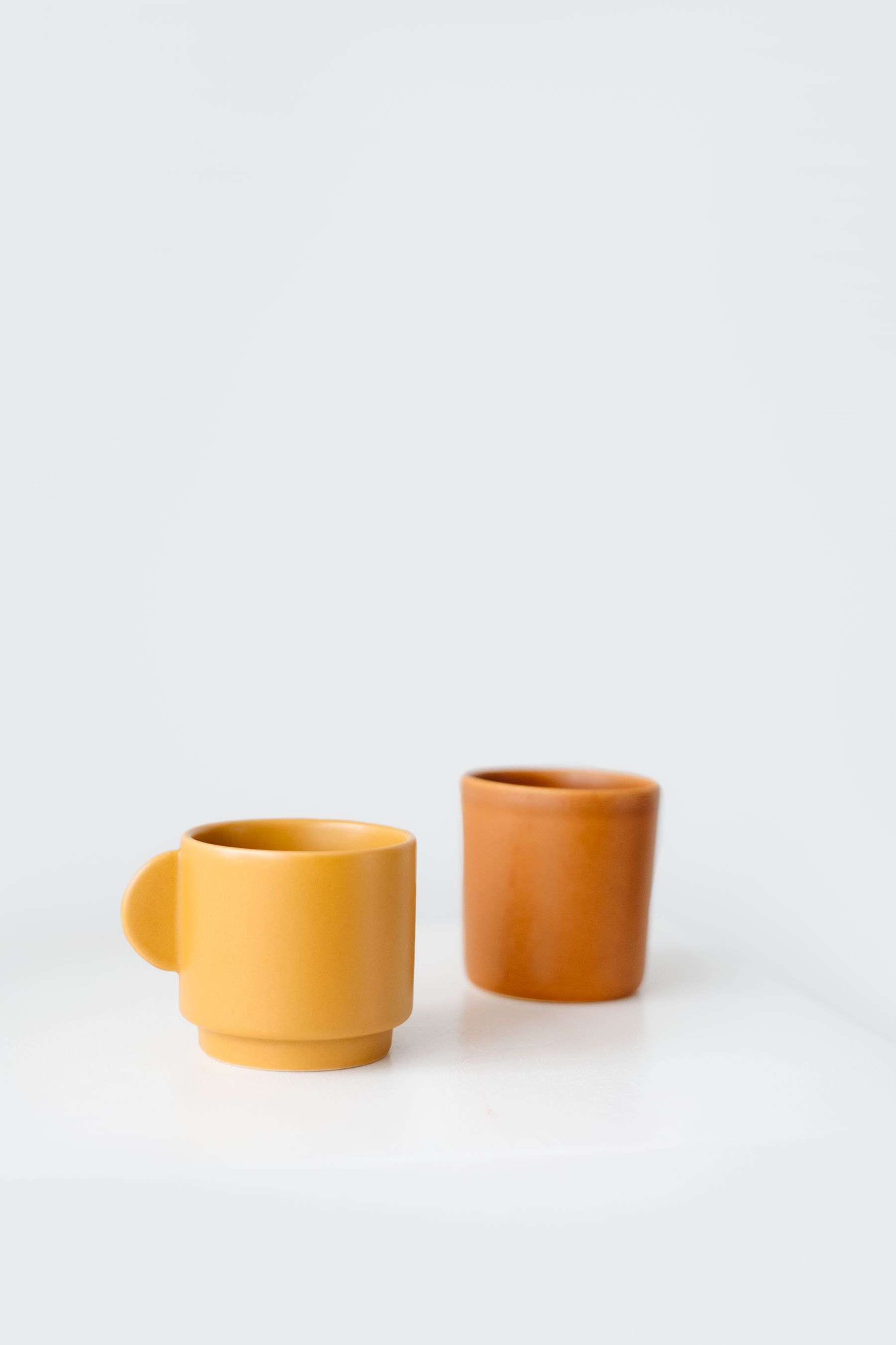 Two small ceramic cups in marigold and burnt orange glaze on a white table