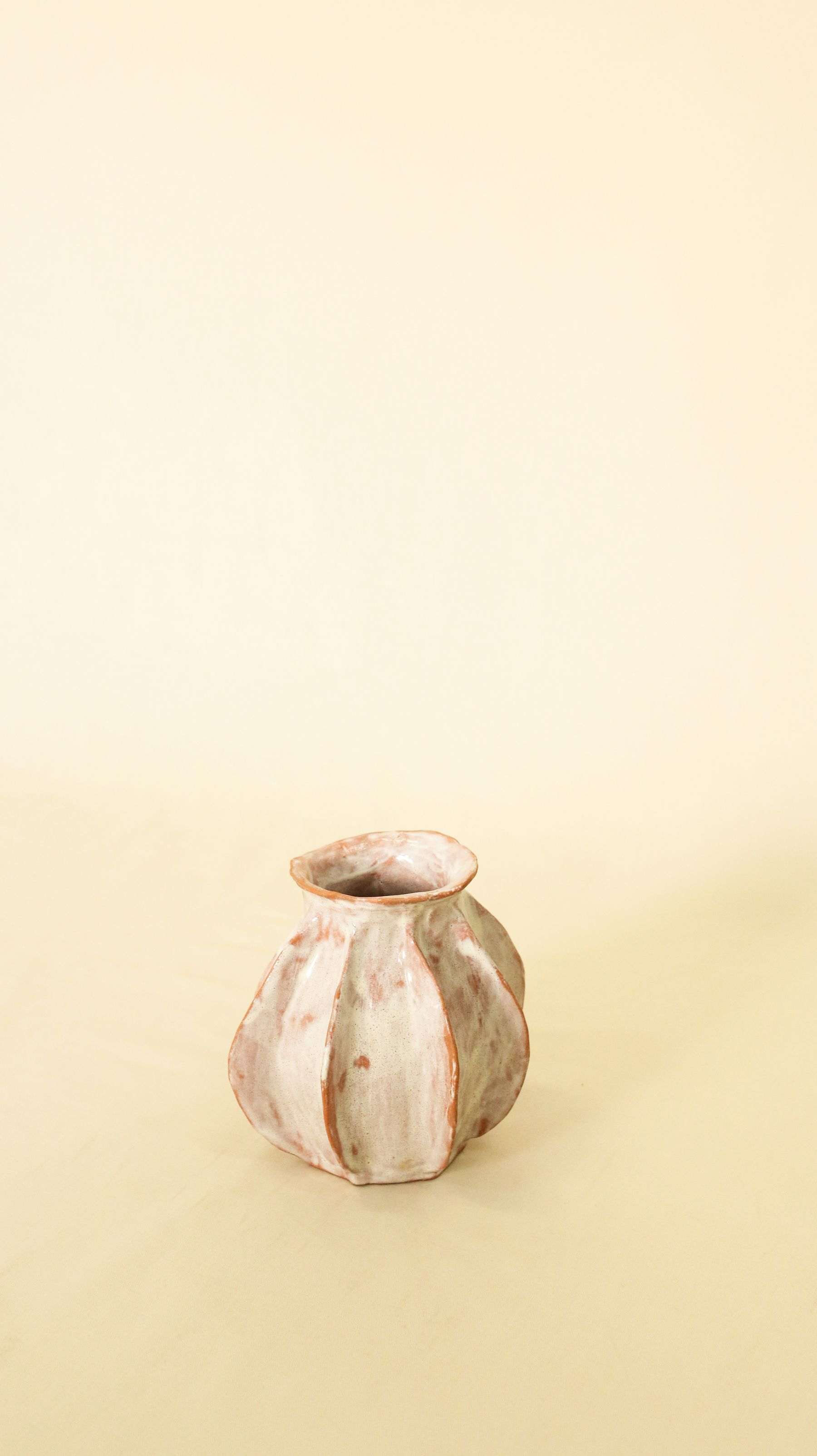 A small ribbed ceramic bud vase with blush and cream glaze on a pale yellow surface