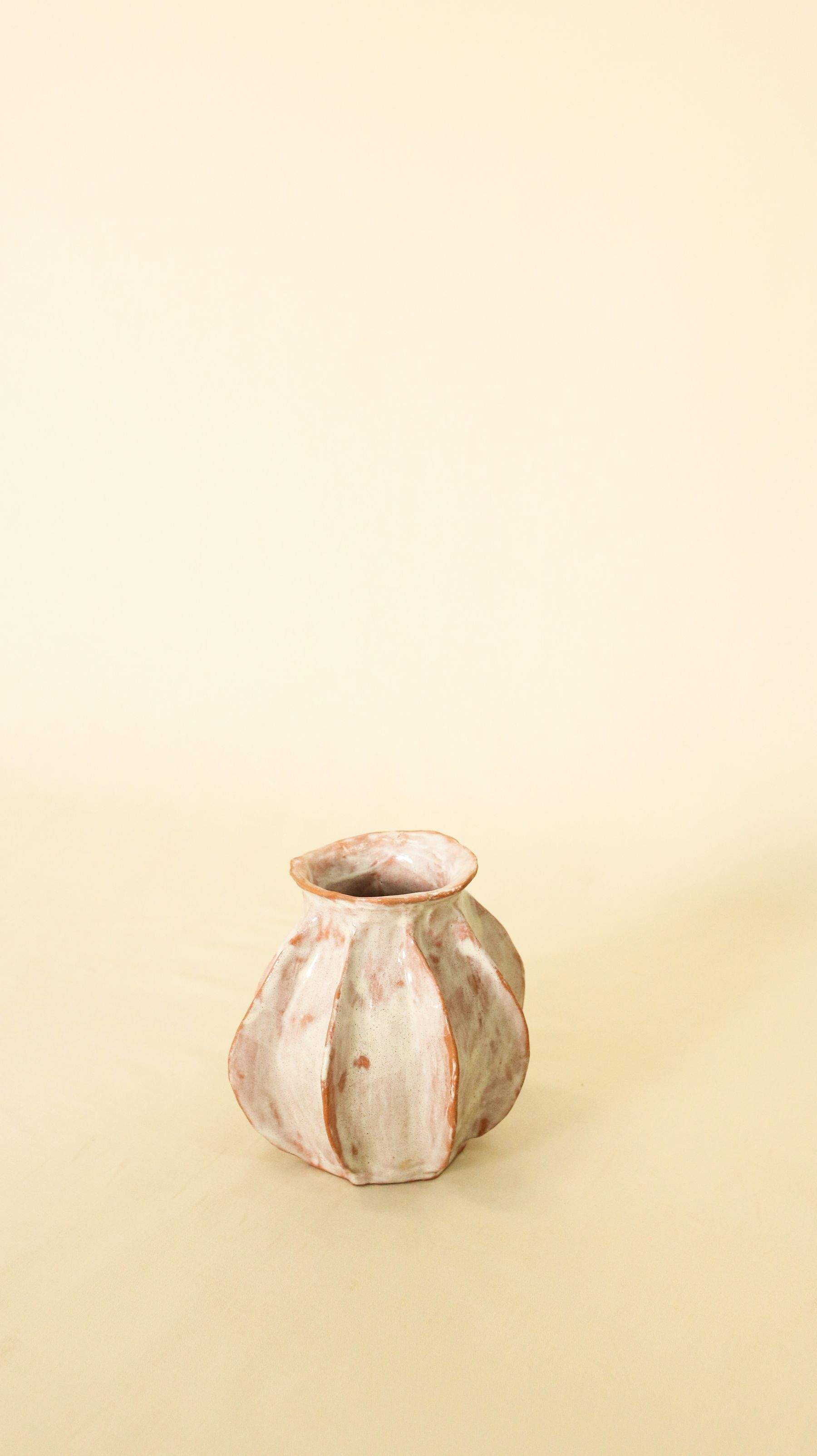 A small ribbed ceramic bud vase with blush and cream glaze on a pale yellow surface